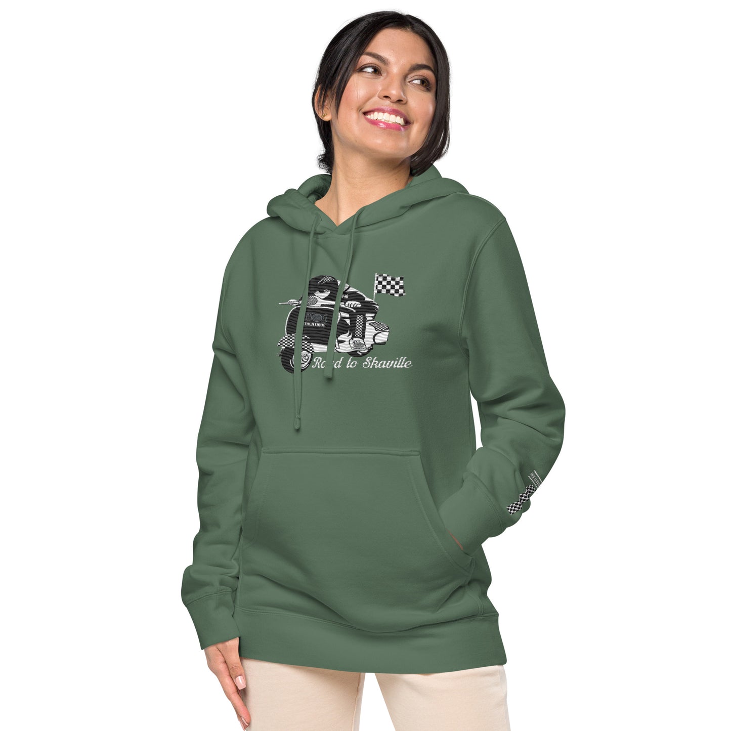 View of a person wearing a green pigment-dyed hoodie with front and sleeve embroidery featuring a vintage moped design and the text 'Road to Skaville'.
