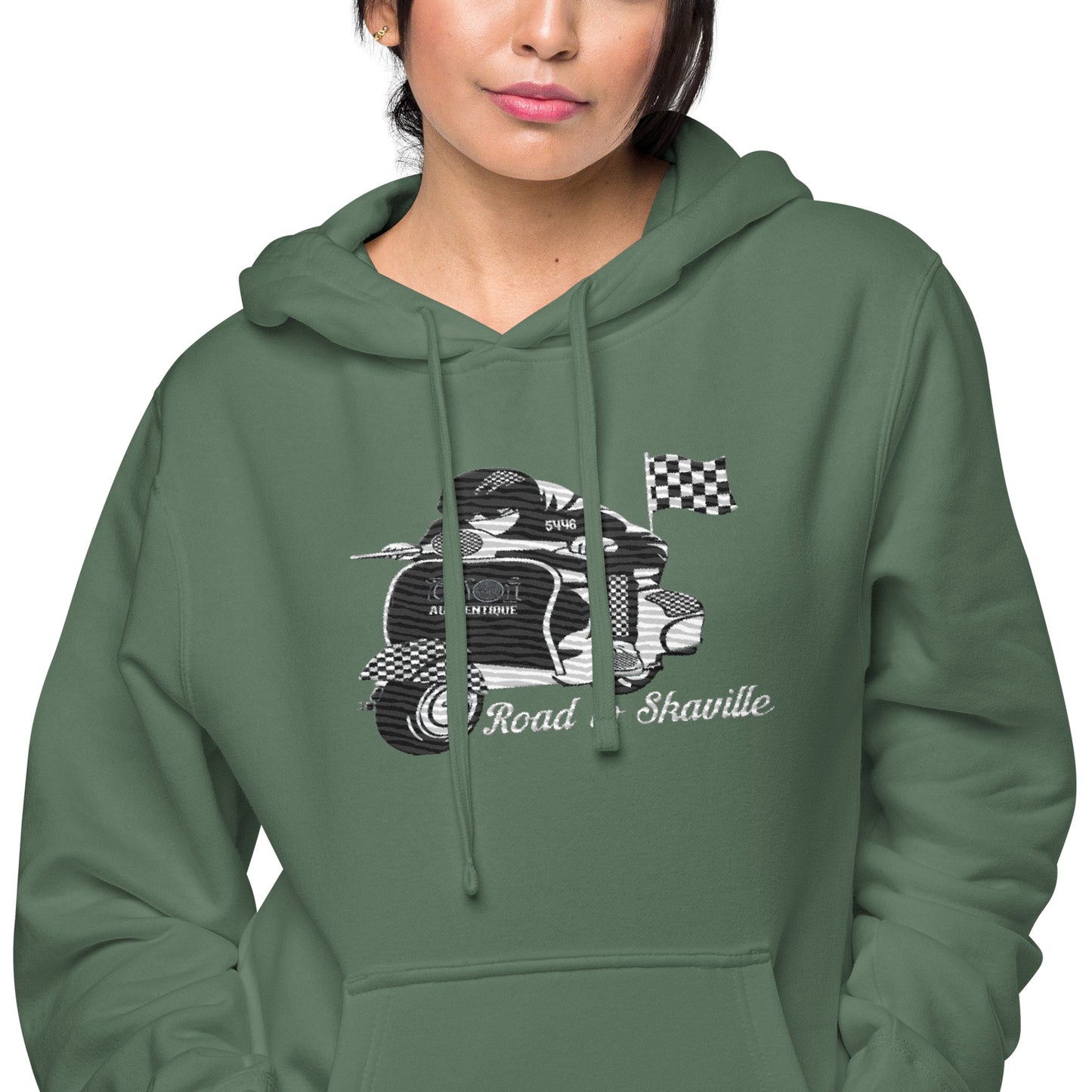 Close-upof a person wearing a green pigment-dyed hoodie with front and sleeve embroidery featuring a vintage moped design and the text 'Road to Skaville'.