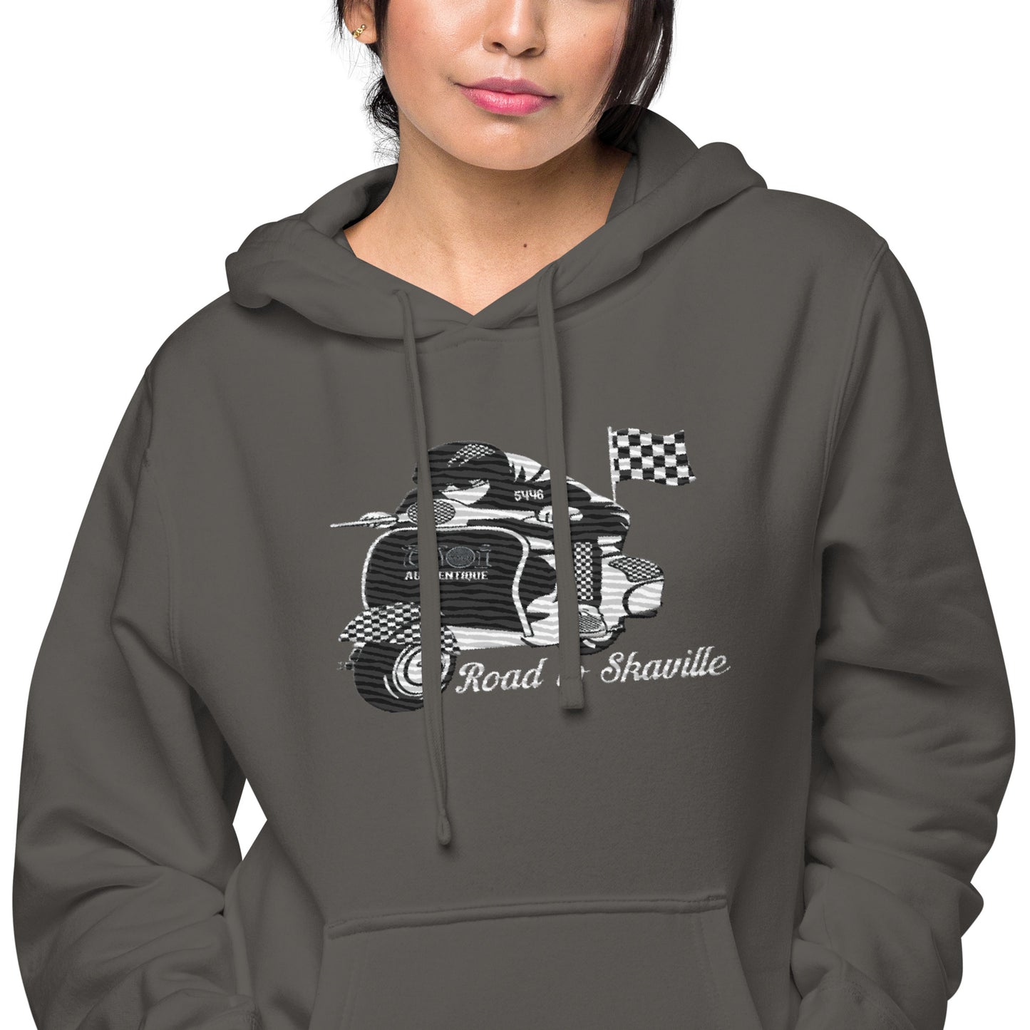 A woman wearing a black pigment-dyed hoodie with front and sleeve embroidery featuring a vintage moped design and the text 'Road to Skaville'.