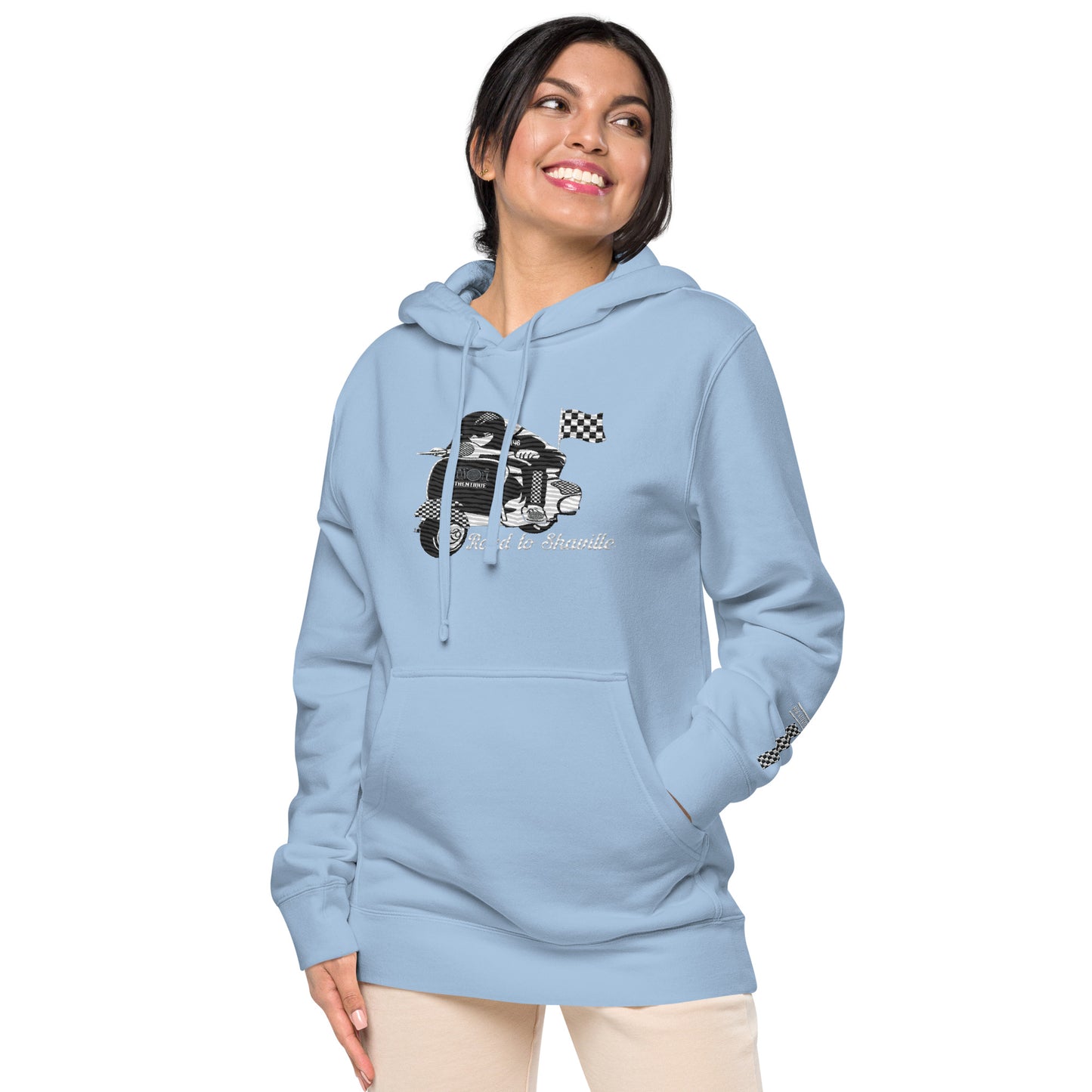 A woman wearing a light blue pigment-dyed hoodie with front and sleeve embroidery featuring a vintage moped design and the text 'Road to Skaville'.