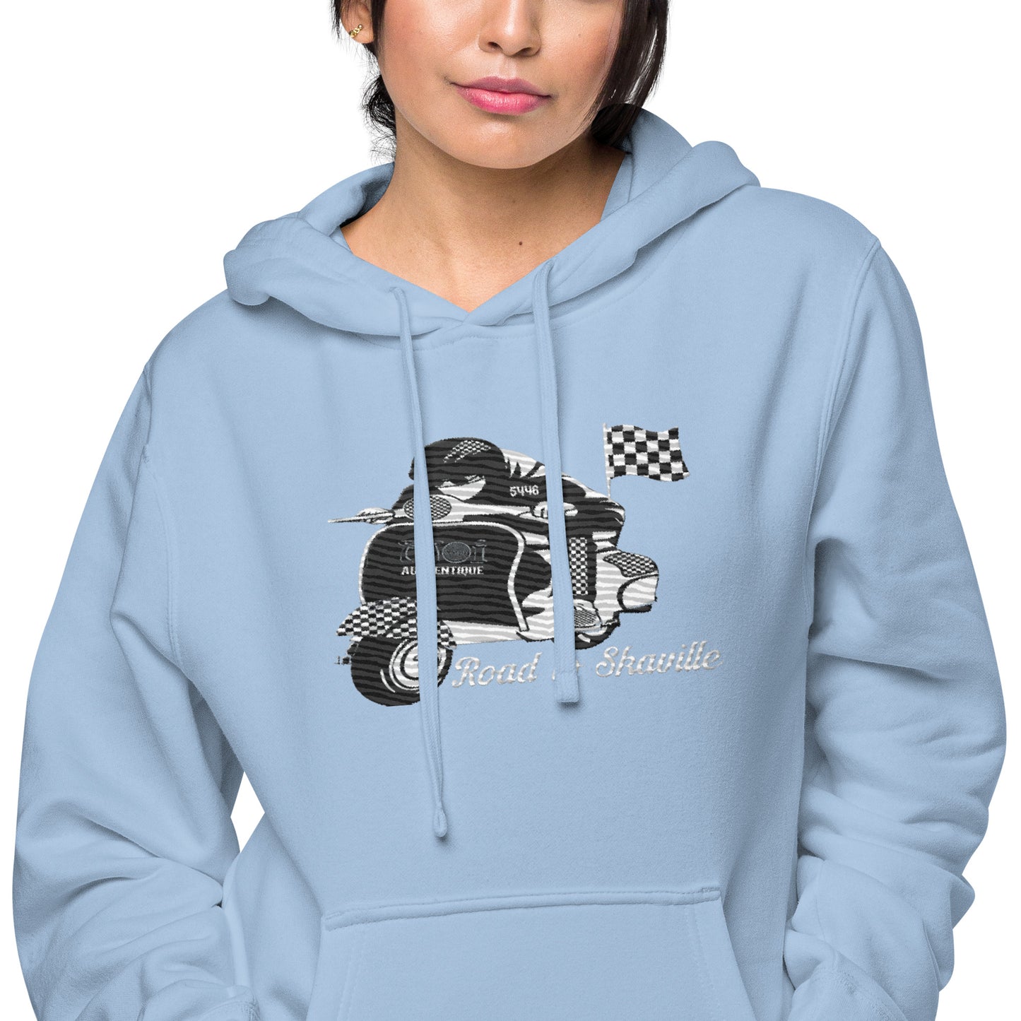 A woman wearing a light blue pigment-dyed hoodie with front and sleeve embroidery featuring a vintage moped design and the text 'Road to Skaville'.