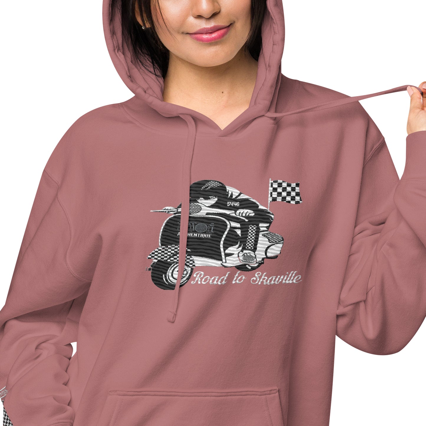 A woman wearing a maroon pigment-dyed hoodie with front and sleeve embroidery featuring a vintage moped design and the text 'Road to Skaville'.