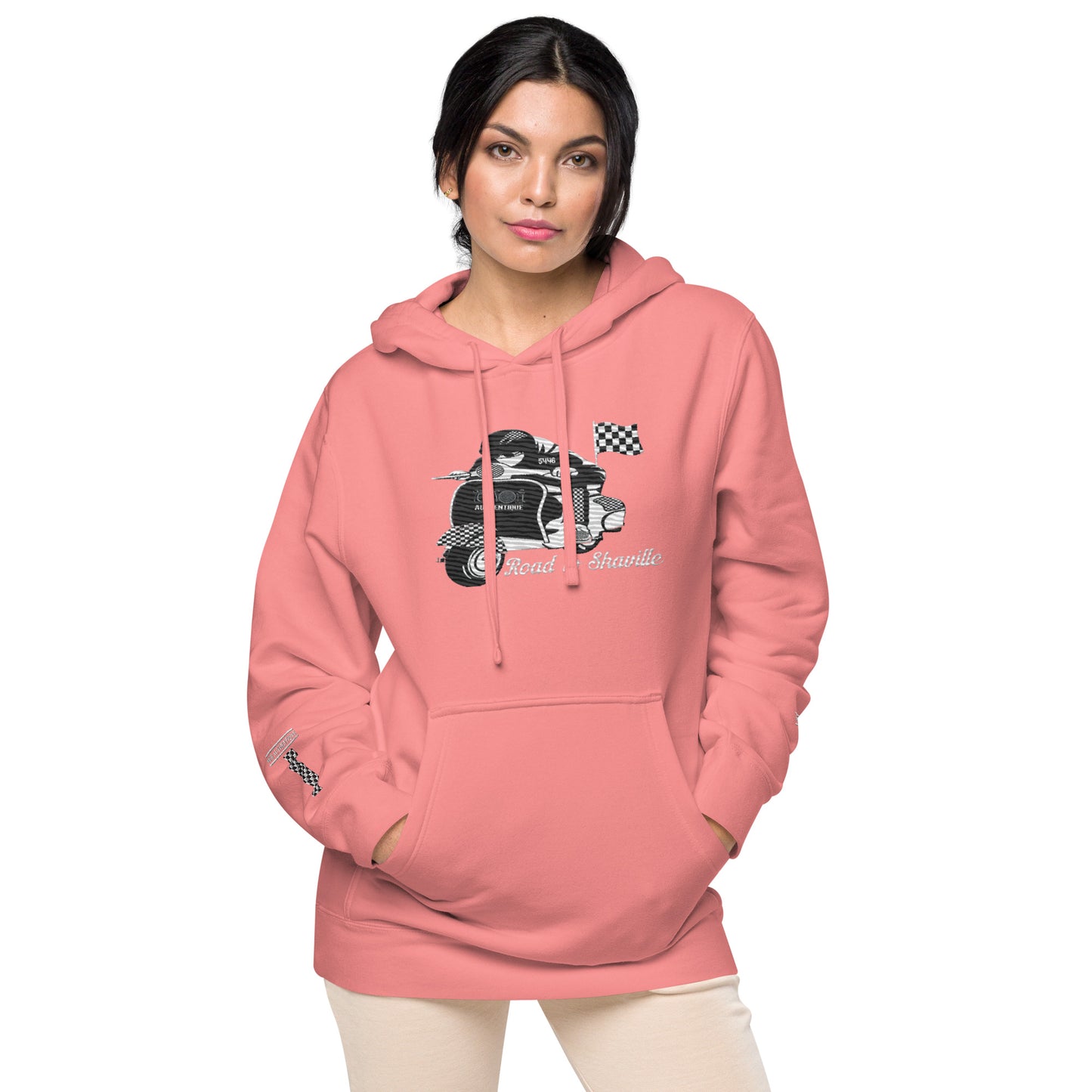 A woman wearing a pink pigment-dyed hoodie with front and sleeve embroidery featuring a vintage moped design and the text 'Road to Skaville'.