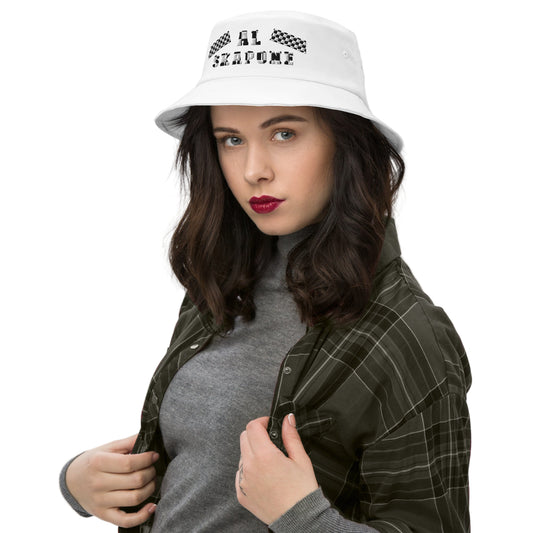 A woman wearing a white embroidered bucket hat with text on it, over a grey top and a checkered jacket.