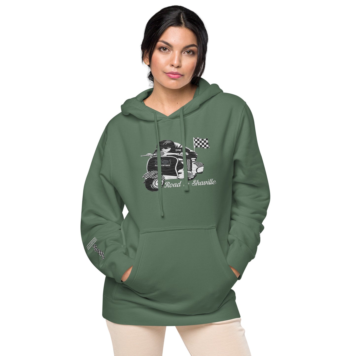 A person wearing a green pigment-dyed hoodie with front and sleeve embroidery featuring a vintage moped design and the text 'Road to Skaville'.