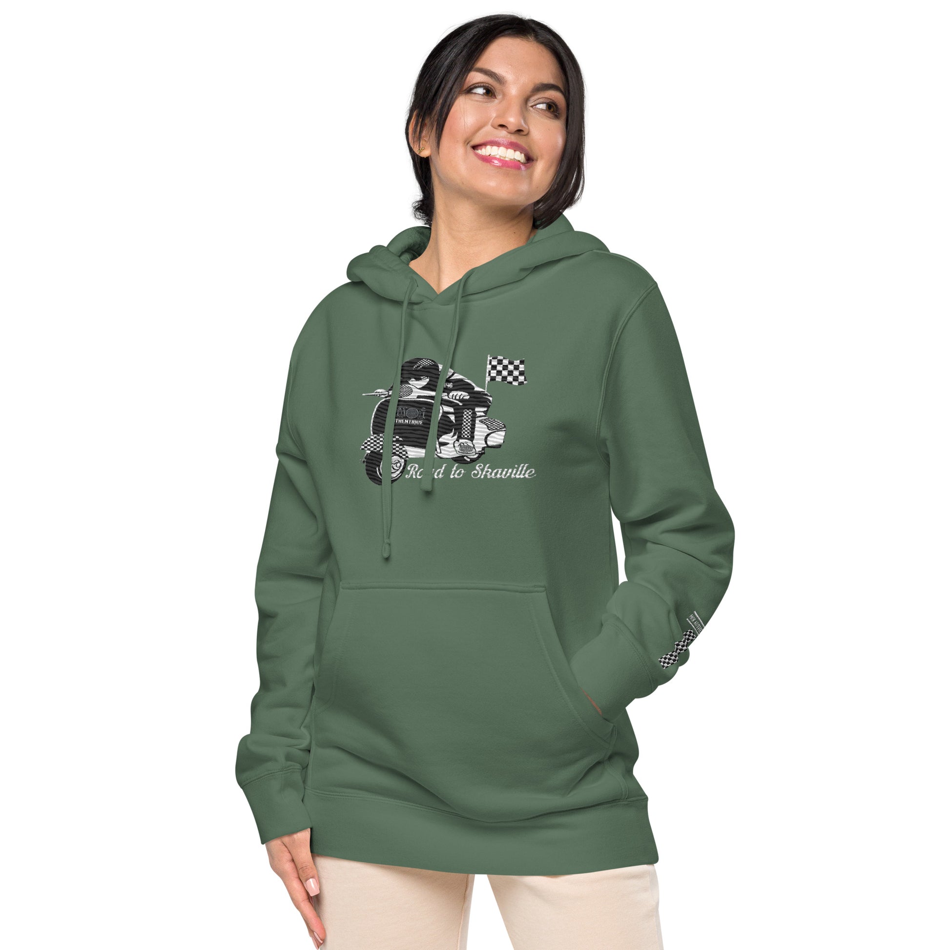 View of a person wearing a green pigment-dyed hoodie with front and sleeve embroidery featuring a vintage moped design and the text 'Road to Skaville'.
