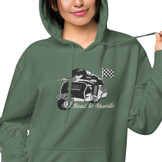 A person wearing a green pigment-dyed hoodie with front and sleeve embroidery featuring a vintage moped design and the text 'Road to Skaville'.