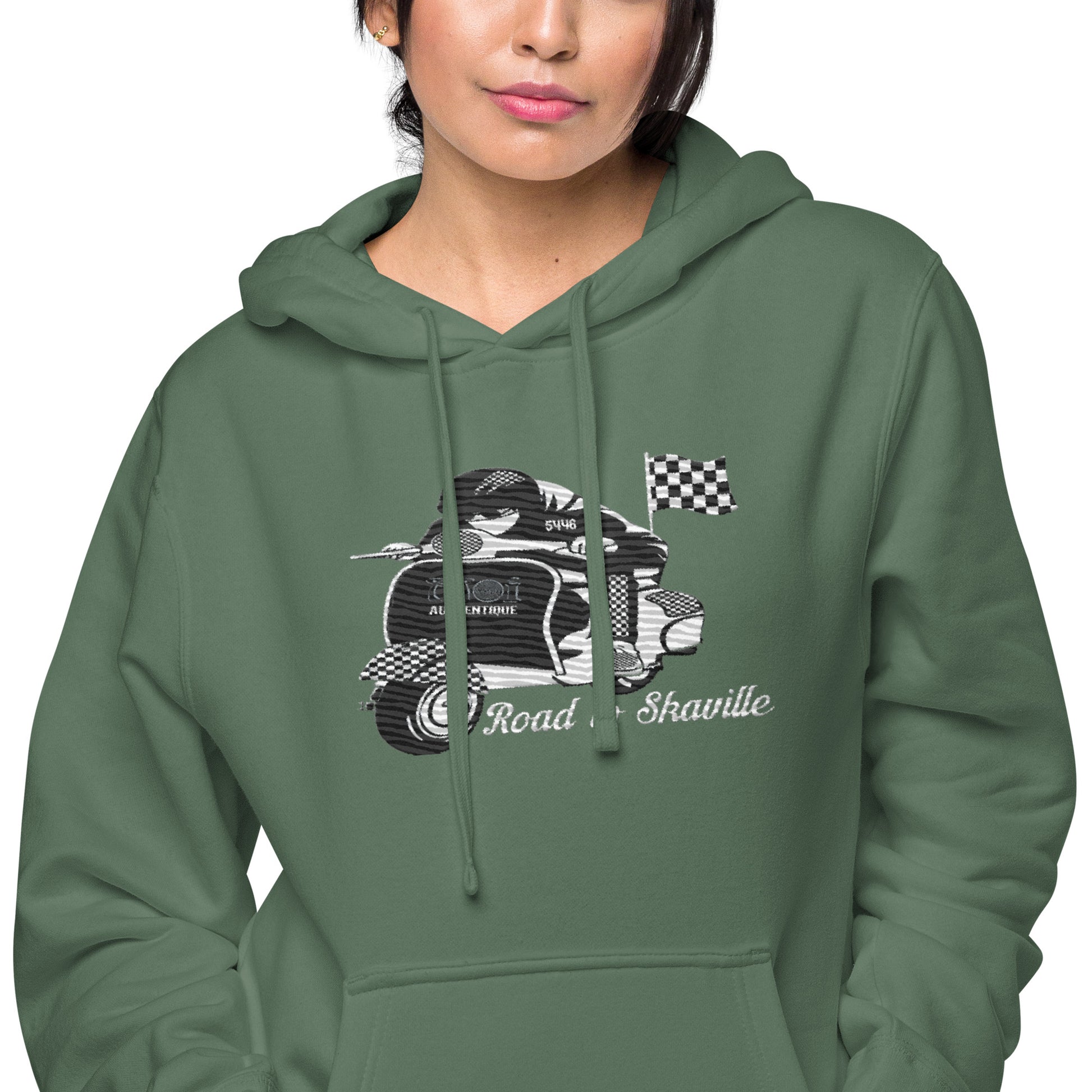 Close-upof a  person wearing a green pigment-dyed hoodie with front and sleeve embroidery featuring a vintage moped design and the text 'Road to Skaville'.