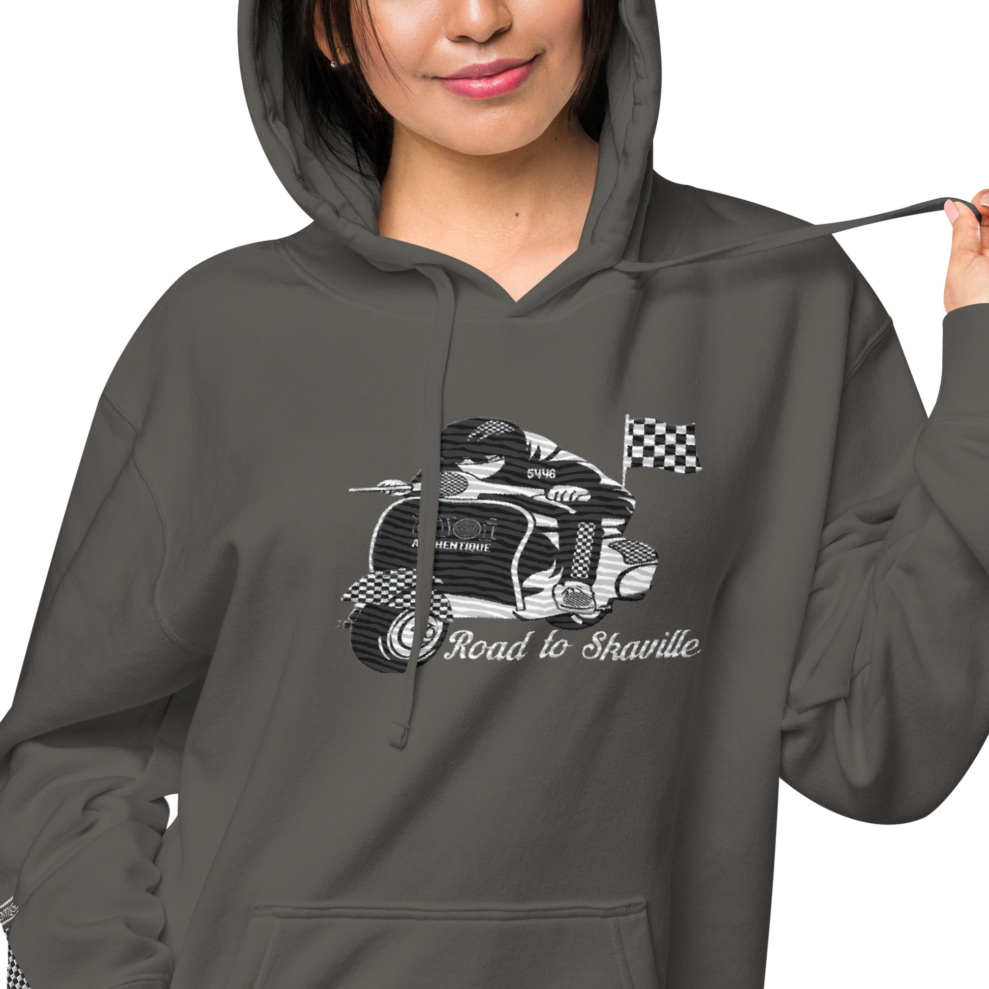 A woman wearing a black pigment-dyed hoodie with front and sleeve embroidery featuring a vintage moped design and the text 'Road to Skaville'.
