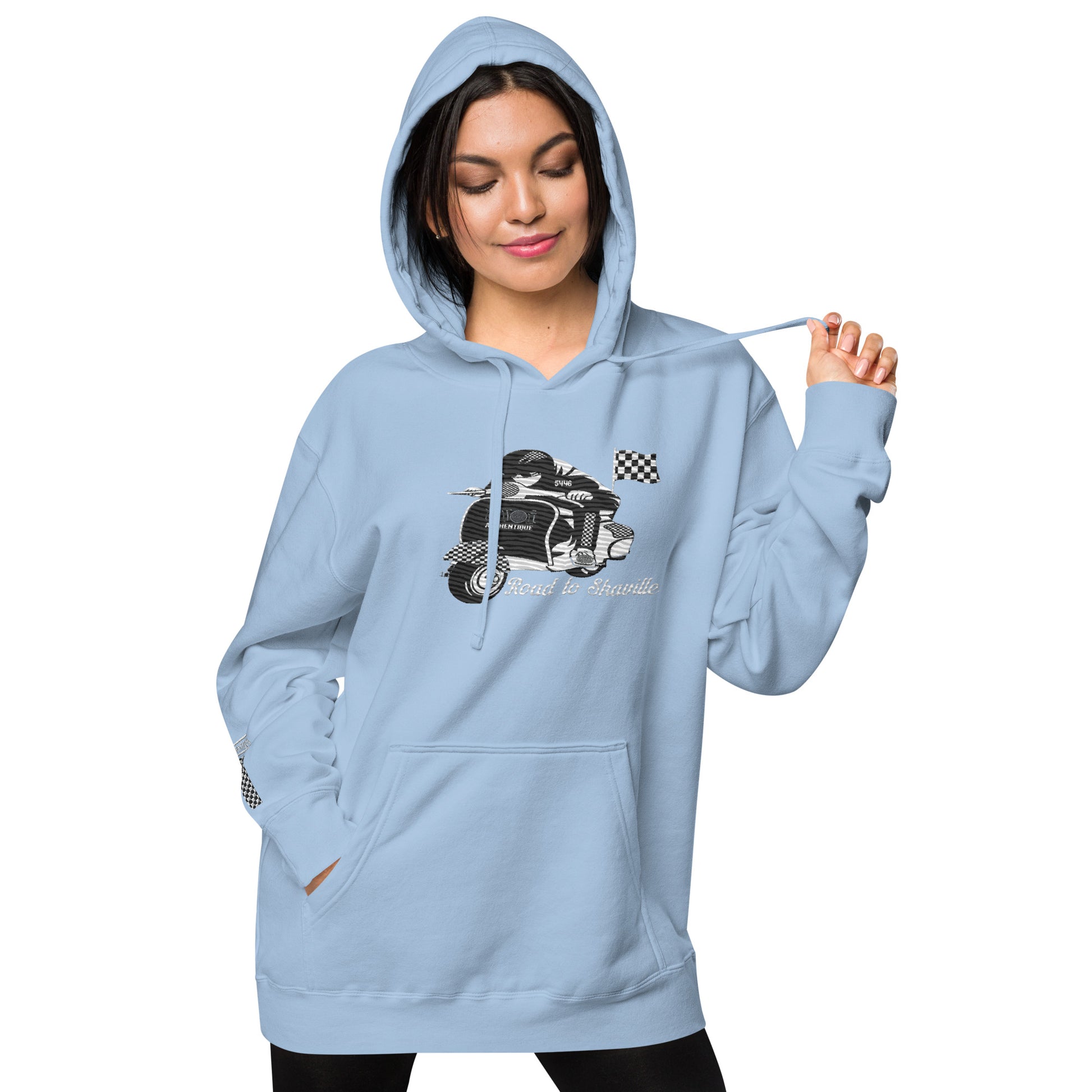 A woman wearing a light blue pigment-dyed hoodie with front and sleeve embroidery featuring a vintage moped design and the text 'Road to Skaville'.