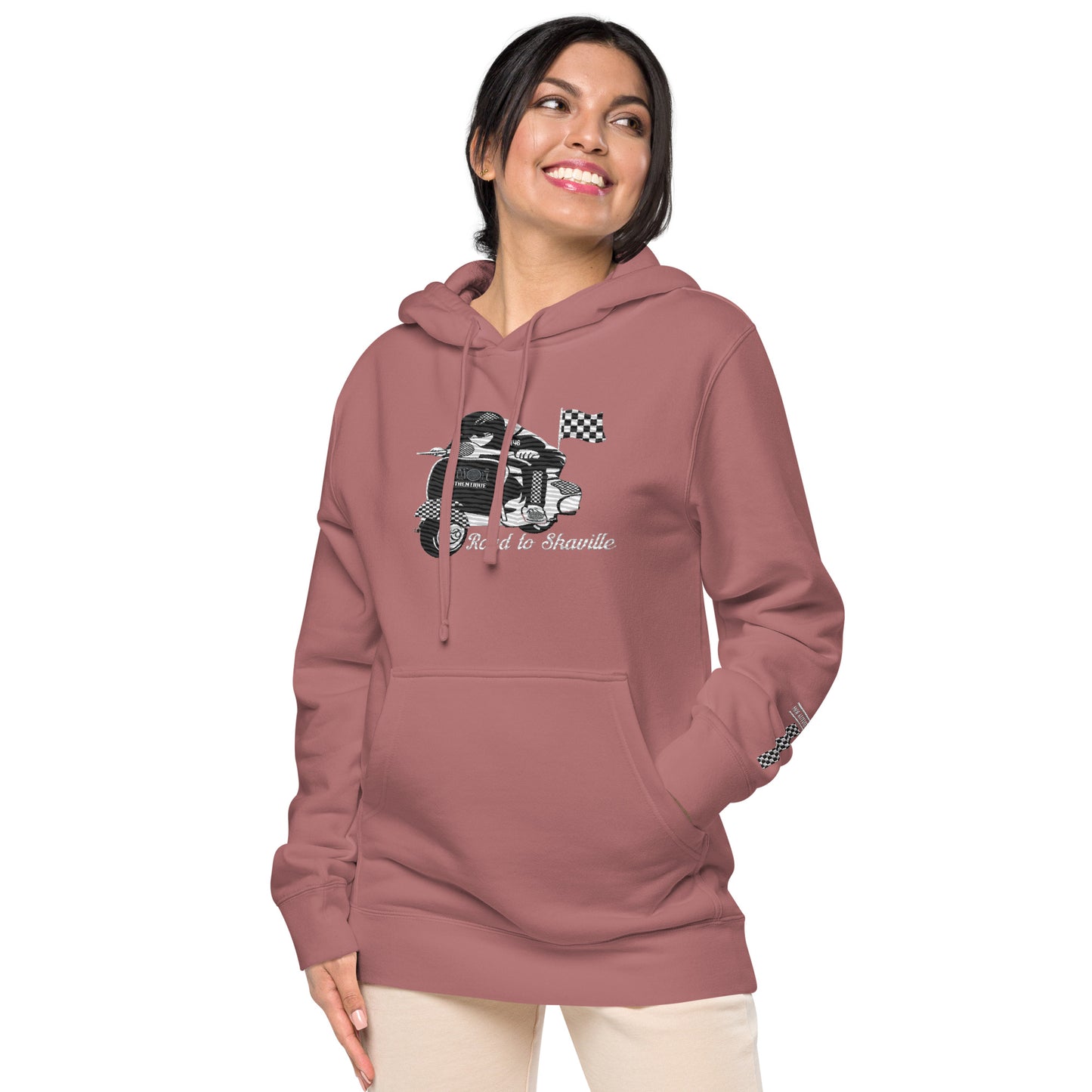A woman wearing a maroon pigment-dyed hoodie with front and sleeve embroidery featuring a vintage moped design and the text 'Road to Skaville'.