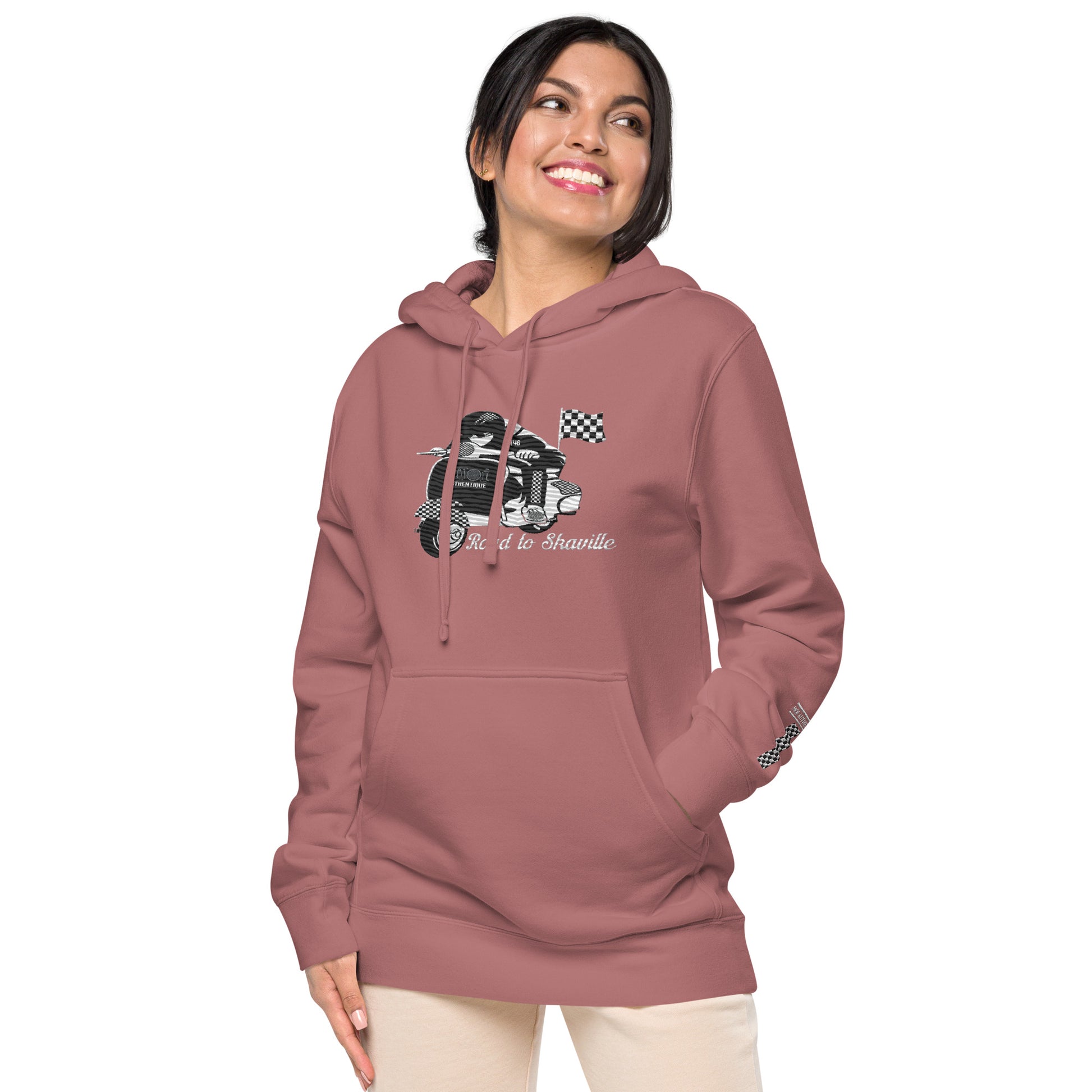 A woman wearing a maroon pigment-dyed hoodie with front and sleeve embroidery featuring a vintage moped design and the text 'Road to Skaville'.