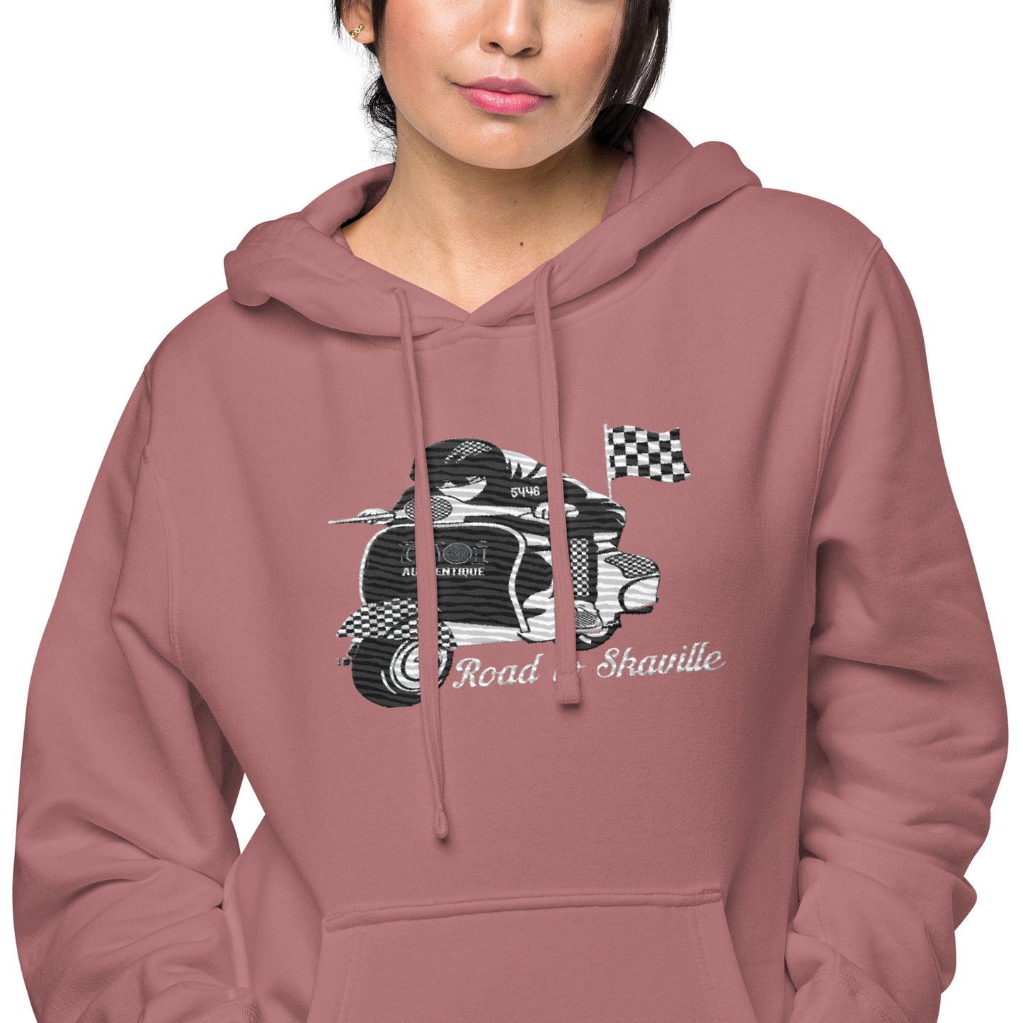 A woman wearing a maroon pigment-dyed hoodie with front and sleeve embroidery featuring a vintage moped design and the text 'Road to Skaville'.