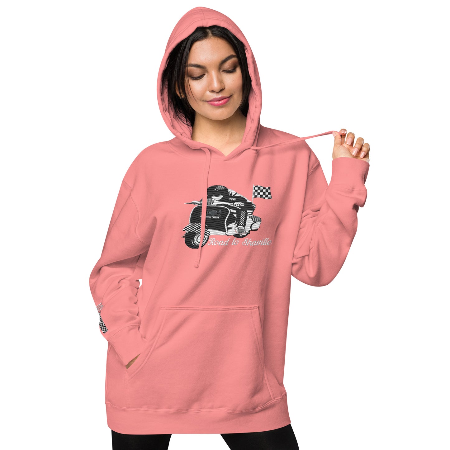 A woman wearing a pink pigment-dyed hoodie with front and sleeve embroidery featuring a vintage moped design and the text 'Road to Skaville'.