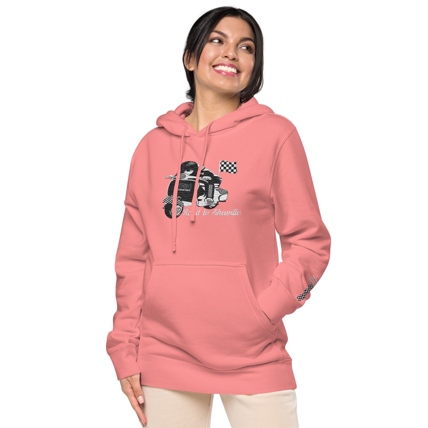 A woman wearing a pink pigment-dyed hoodie with front and sleeve embroidery featuring a vintage moped design and the text 'Road to Skaville'.