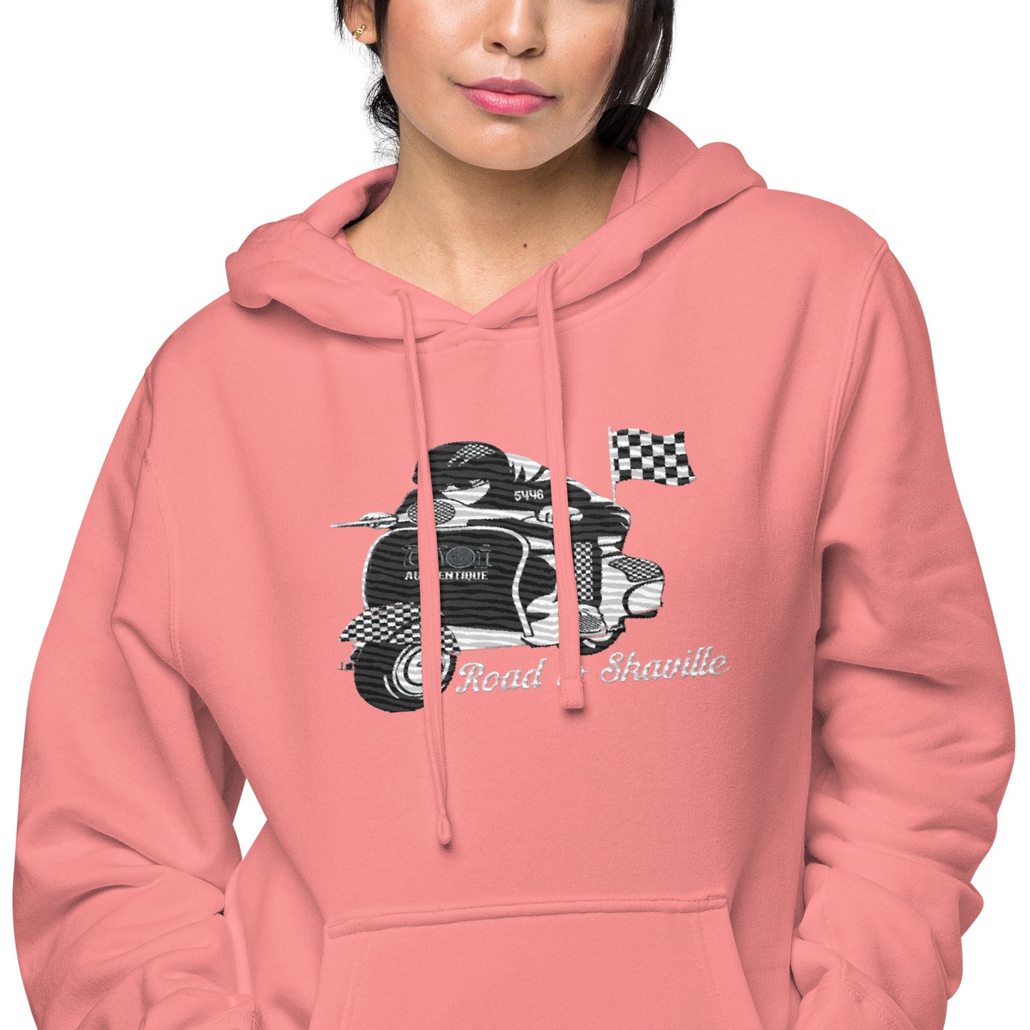 A woman wearing a pink pigment-dyed hoodie with front and sleeve embroidery featuring a vintage moped design and the text 'Road to Skaville'.