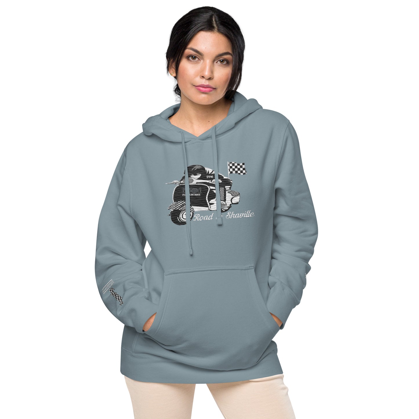 A woman wearing a slate blue pigment-dyed hoodie with front and sleeve embroidery featuring a vintage moped design and the text 'Road to Skaville'.